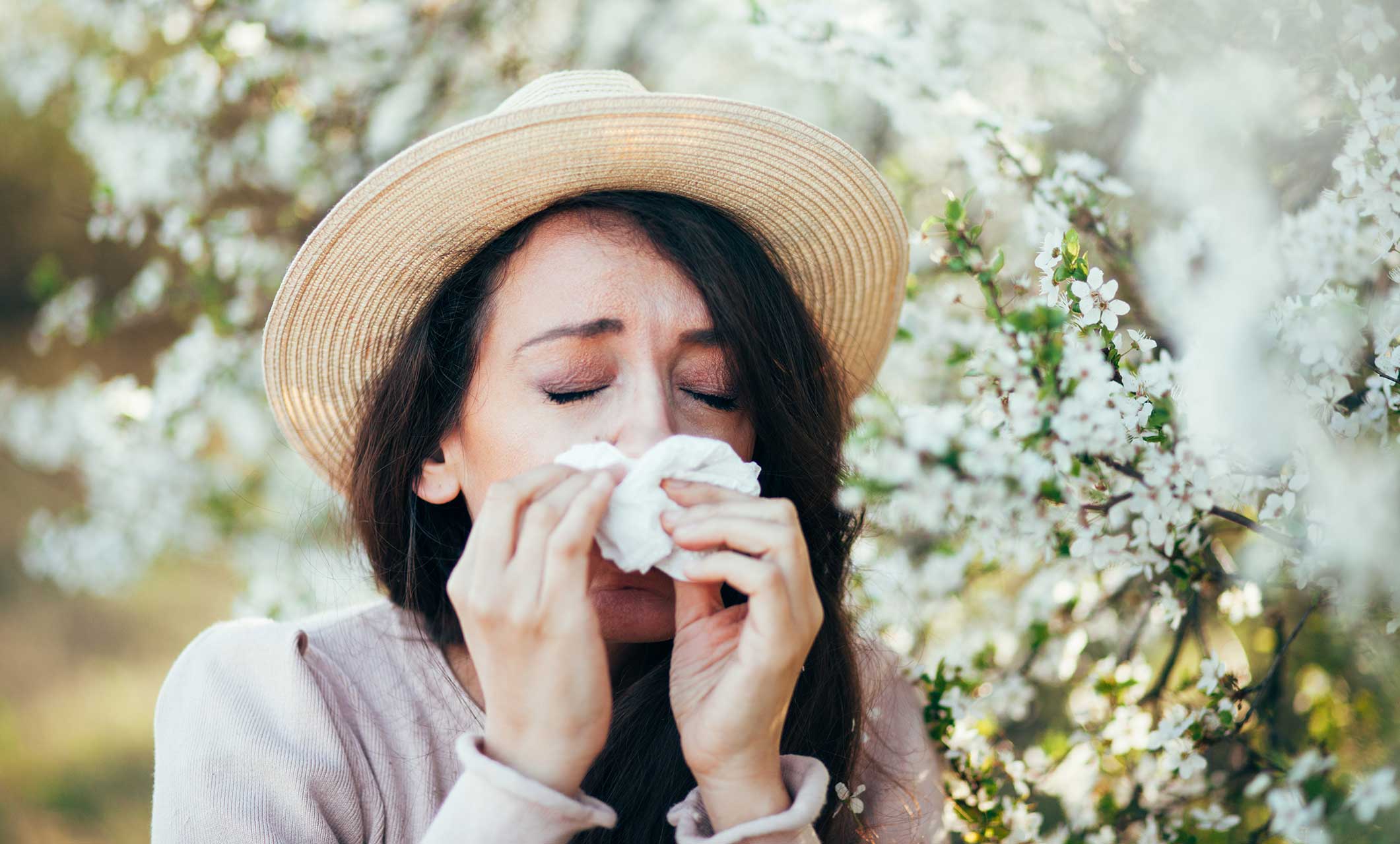 Woman by a flowering tree blowing her nose